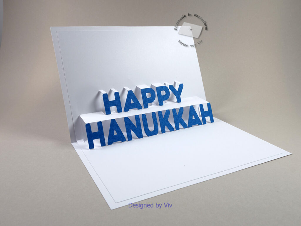 Card shown from an angle with the pop up letters Happy Hanukkah. Blue letters are glued to each individual pop up letter.