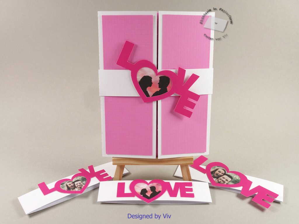 A gatefold card shown closed with a belly band with the word love diagonally across it. The O of the Love is replaced with a heart frame where a photo can be placed. Three other variations of the belly band and the Love photo frame lie in front.